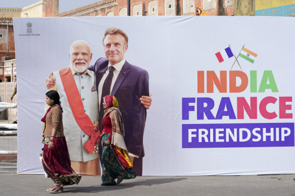 Women walk past a billboard showing French President Emmanuel Macron with Indian Prime Minister Narendra Modi in Jaipur, Rajasthan.