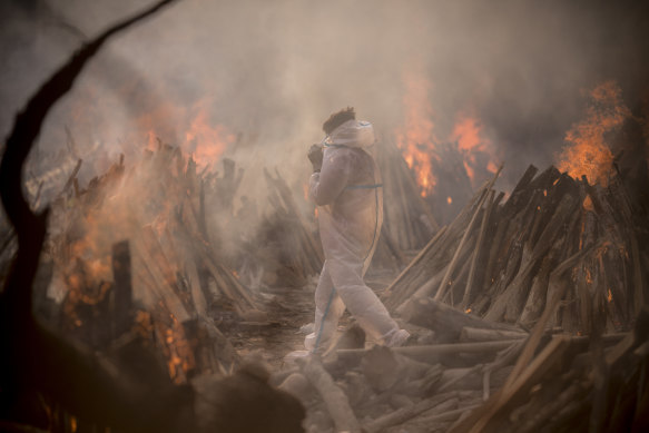 A worker wearing a protective suit is seen amid the burning funeral pyres of patients who died of COVID-19 at a crematorium in Delhi, India.