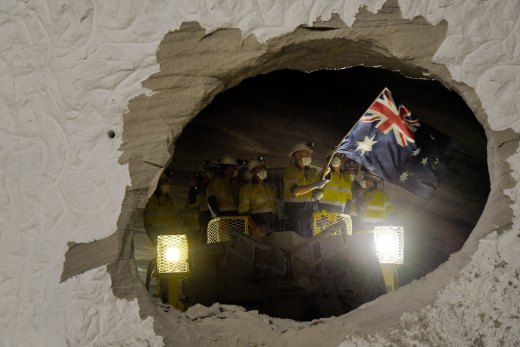 A worker on one of the two roadheaders waves the Australian flag moments after smashing through sandstone connecting two sections of the M4-M5 Link.