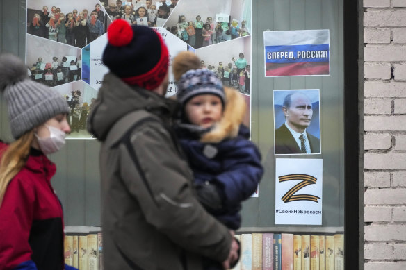 A family walks past a portrait of Russian President Vladimir Putin, displayed in the window of a children’s library in St. Petersburg.