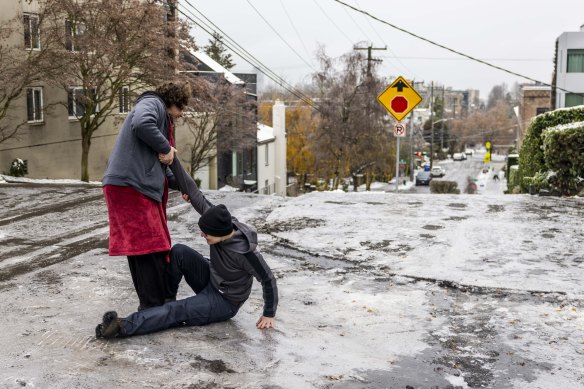     Garrett Fuller (left) helps his friend Robin Jacobs get up after slipping on the icy ground of Capitol Hill in Seattle.