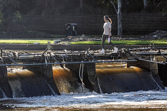 A woman walks across piles of debris left by the recently flooded Parramatta River