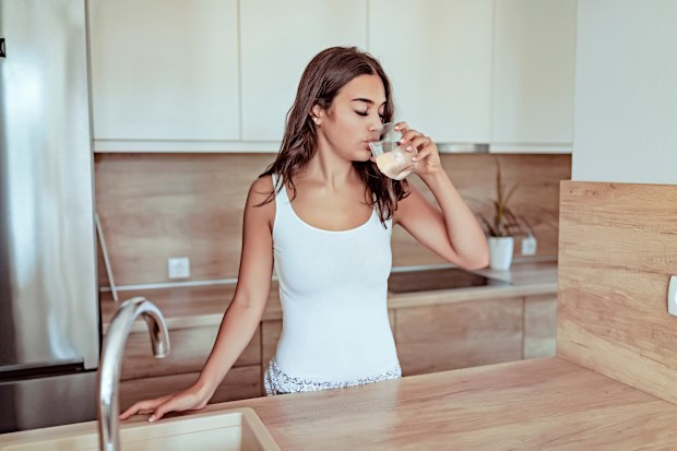 Portrait of Young Woman Holds a Glass With Water Against Kitchen Background. Content Cute Girl Drinking a Glass of Water at Home at Early Morning in Her Modern Kitchen