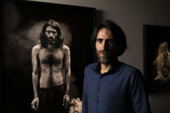 Behrouz Boochani  stands in front of a portrait of himself, part of Hoda Afshar’s Remain series.