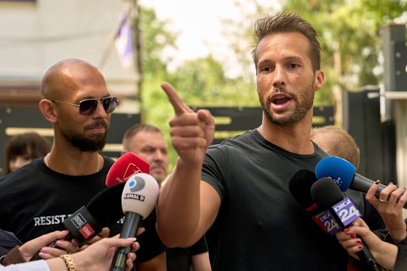 Tristan Tate speaks outside a police station as his brother Andrew watches.