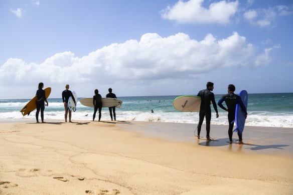 Surfers stand along the beach as they assess the surf.