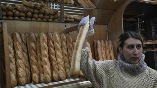 Mylene Poirier talks to a customer as she takes a baguette at a bakery, in Versailles, west of Paris.