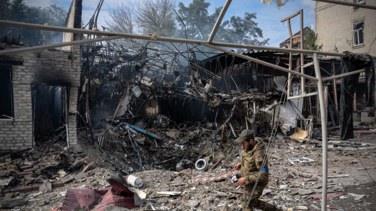 A soldier passes the crater where a Russian missile struck a shopping area earlier in the day in Kupiansk.