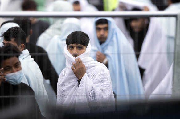 Migrant men wrapped in a blankets are kept behind barriers at the Manston airfield migrant processing centre.