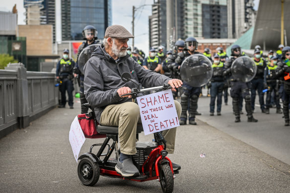 Catholic priest Peter Murnane attend the protest with a sign on his mobility scooter. 