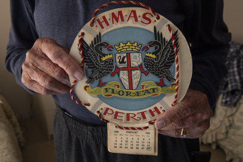 WW2 veteran Frank McGovern holding a 1942 HMAS Perth calender, the date of the bombing of the ship is marked.