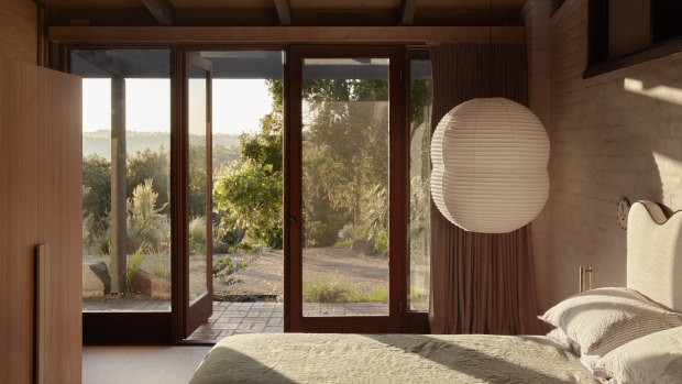 In the main bedroom, floor-to-ceiling windows connect to the landscape while the bagged brick wall frames an over-scale paper lantern.