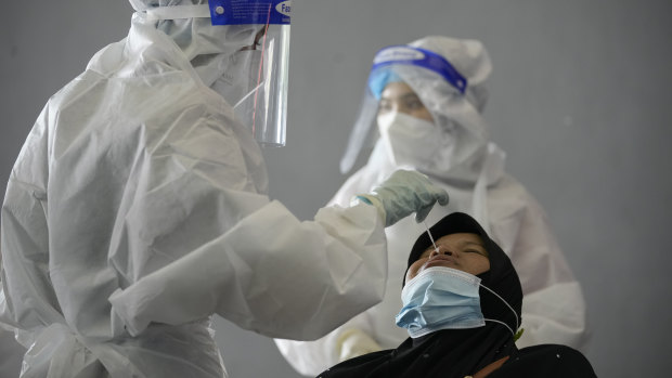 A medical worker collects swab sample from a woman during coronavirus testing at a COVID-19 testing center in Shah Alam, outskirts of Kuala Lumpur, Malaysia,