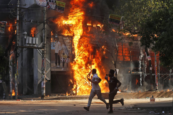 Men run past a shopping centre, which was set on fire by protesters during a rally against Bangladesh’s Prime Minister Sheikh Hasina and her government demanding justice for the victims killed in the recent countrywide deadly clashes, in Dhaka.