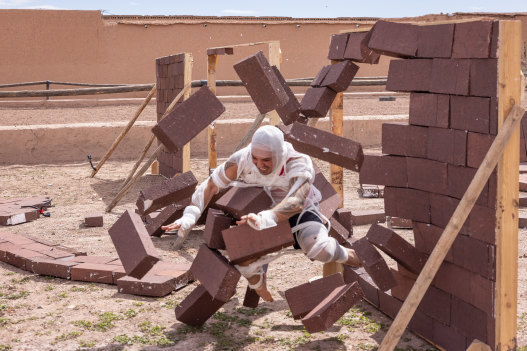 A contestant crashes through a brick wall as part of a challenge in the 2022 season of The Amazing Race.