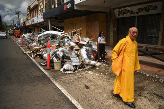 A Buddhist monk, part of a group visiting flood affected areas and donating money to victims, walks past a pile of debris in the Lismore central business district on Tuesday morning.