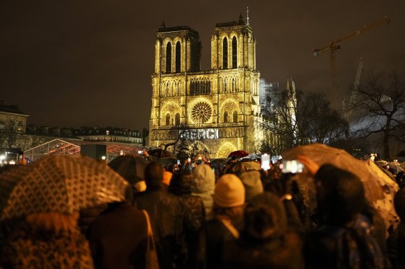 Merci – thank you – is projected onto the facade of the cathedral as spectators gather outside. 
