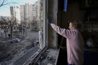 A woman measures a window before covering it with plastic sheets in a building damaged by a bombing in Kyiv