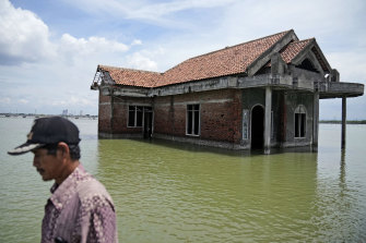 A man walks past a house abandoned after it was inundated by water due to the rising sea level in Sidogemah, Central Java, Indonesia, Monday, November 8, 2021. 