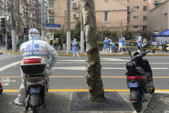 A police officer in protective gear watches over residents lining up for COVID tests in the Jingan district of western Shanghai.