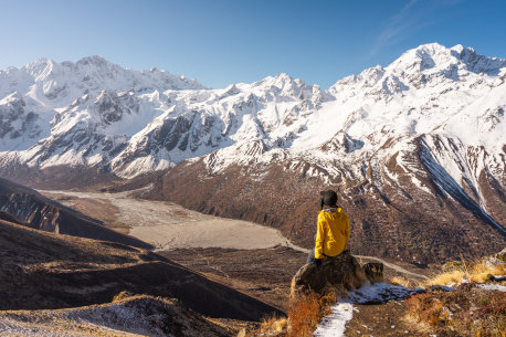 A trekker sitting on top of Kyanjo Ri view point and enjoying landscape of Langtang valley. Himalaya mountains range in Nepal, Asia Cover: Nepal: trekking a decade on from the earthquake text by Andrew Bain