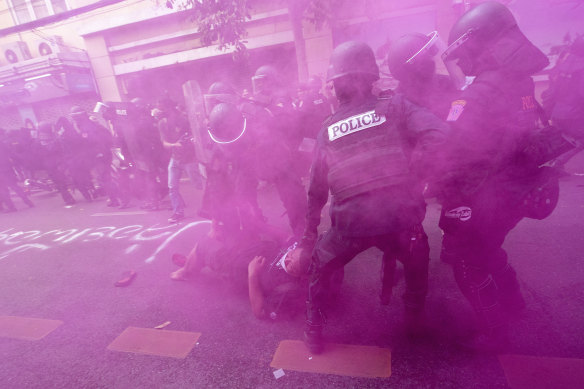 In cloud of pink smoke, police in riot gear remove a protester trying to march to the Asia-Pacific Economic Cooperation APEC summit venue in Bangkok on Friday.