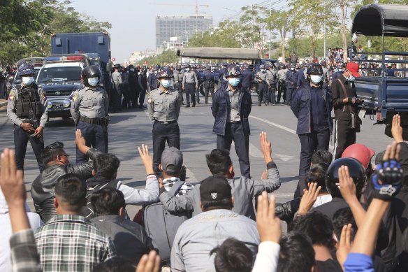 Protesters sit on a road blocked by police as they flash a three-fingered salute, a symbol of resistance, during a protest in Mandalay.