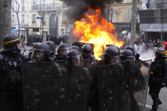 Riot police officers stand by a burning car during clashes at a demonstration against plans to push back France’s retirement age, in Paris on Saturday, February 11.