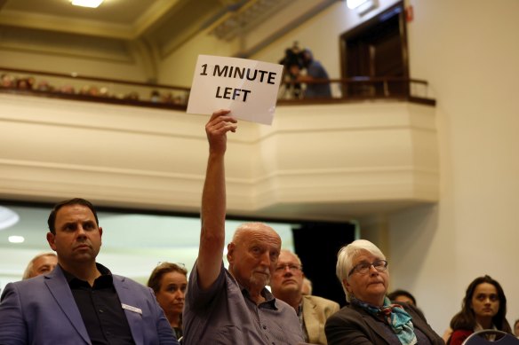 A moderator holds a sign indicating time left for a speaker during debate at Brighton Town Hall.