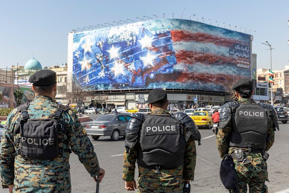 Riot police stand in front of a giant anti-US billboard depicting the destruction of a US aircraft carrier in downtown Tehran.