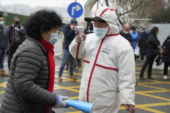 A worker in protective overalls takes the temperature of a woman entering the Hubei Centre for Disease Control and Prevention as the World Health Organisation team makes a visit.