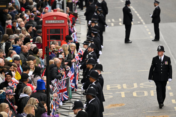 Police officers stand on patrol as well-wishers line the procession route ahead of the coronation.