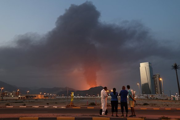 Foreign workers look at a tall plume of black smoke ascends following an explosion in the Fujairah industrial zone on March 3, 2026.