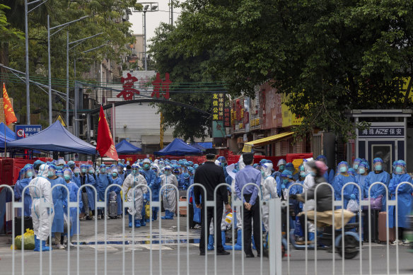 Police, in white PPE, prepare to transfer residents, in blue PPE, from a village following a high number of COVID infections in Guangzhou.