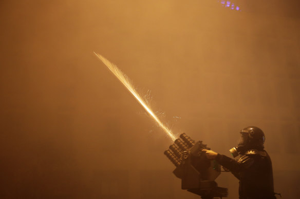 A riot police officer fires on protesters with a tear-gas launcher.