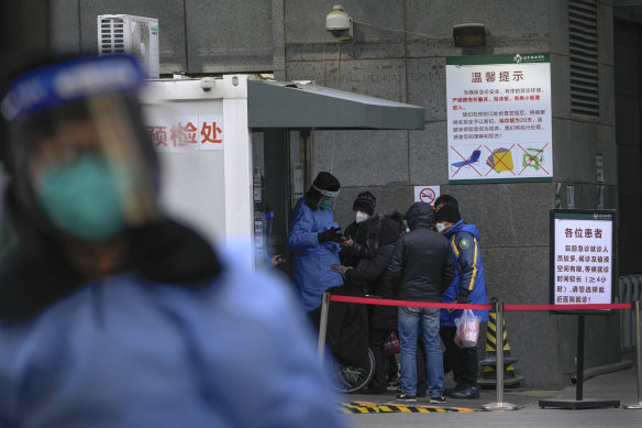 A worker in protective gear checks on residents’ reservations outside a hospital in Beijing on Thursday.