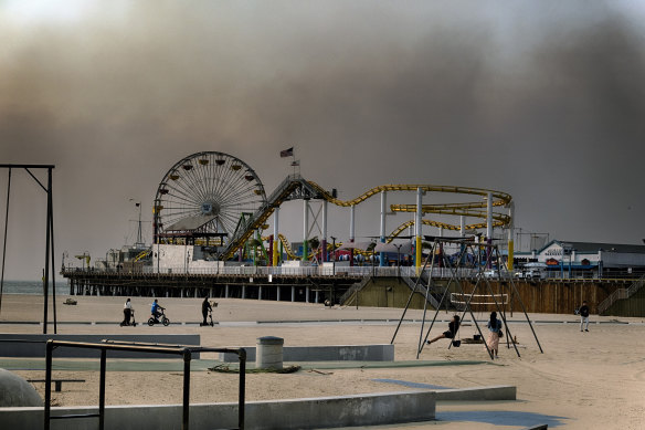 People play on the beach as smoke from a wildfire blows over the Santa Monica Pier on Wednesday. 