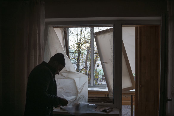 A man uses plastic to cover a broken window in his apartment following a Russian drone attack in Kyiv.