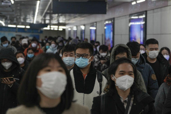 Masked commuters walk through a walkway in between two subway stations as they head to work during the morning rush hour in Beijing,