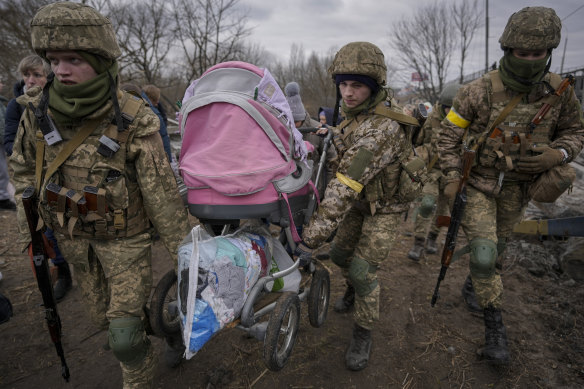 Ukrainian servicemen carry a baby stroller while assisting people fleeing the town of Irpin, Ukraine.