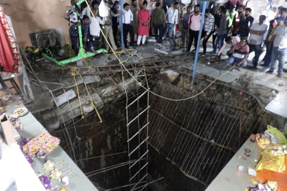 People stand around a structure built over an old temple well that collapsed on Thursday,