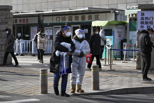 A couple in protective gear stand outside a hospital in Beijing. Beijing is trying to revive the economy as it grapples with a full-blown COVID-19 wave.