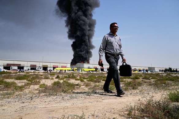 A man walks away after watching a black plume of smoke rising from a warehouse in the industrial area of Sharjah City, United Arab Emirates. 
