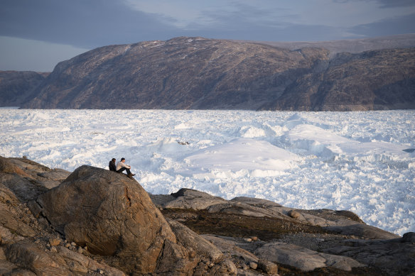 Los investigadores se sientan en una roca con vista al glaciar Helheim en Groenlandia.