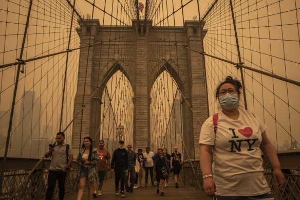 People cross the Brooklyn Bridge amid a dense haze from wildfire smoke in New York.