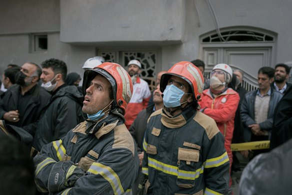 Firefighters look on as volunteers and first responders inspect the rubble and search for victims at a residential building in north-west Iran.