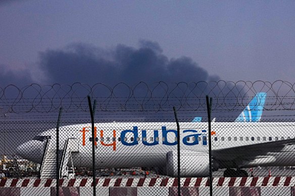 A FlyDubai plane is parked at Dubai International Airport as smoke rises in the background after a drone strike.  