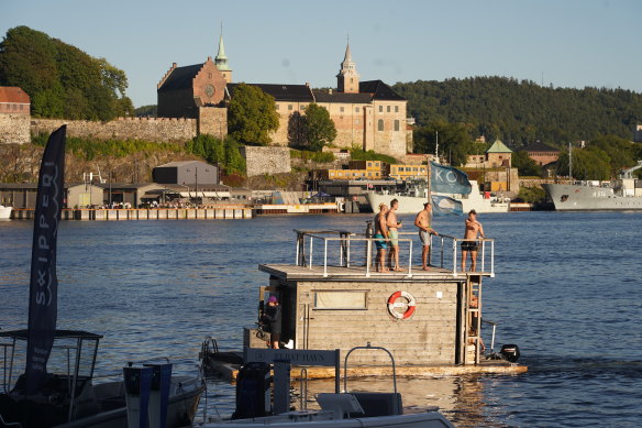 A motorised floating sauna in Oslo passes in front of the Akershaus Fortress .