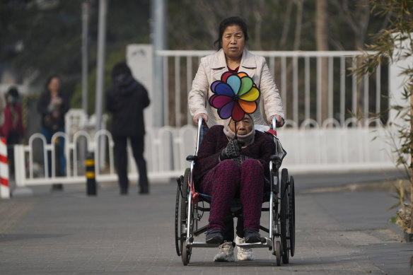 A woman pushes an elderly woman holding a rainbow fan on a street in Beijing. 