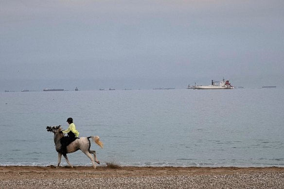 راكب يركض على شاطئ بينما تتراص ناقلات النفط والسفن التجارية في مضيق هرمز بالقرب من خورفكان، الإمارات العربية المتحدة.